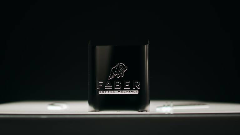 Un fotogramma scuro dello spot: il corpo di una macchina Faber con il logo del toro, su un set nero.